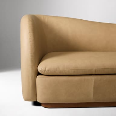 A contemporary two-seater loveseat upholstered in tan leather with a curved back and integrated armrests, resting on a dark wooden plinth base. — 3D model