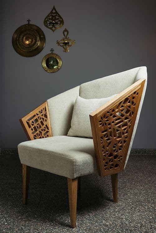 A modern armchair featuring a high, angular backrest and a cushioned seat and back. The armchair has distinctive wooden armrests with intricate geometric cutouts. The legs are tapered and made of wood. — 3D model