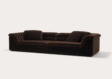 A long, three-seater sofa with a channeled design on the backrests and armrests. The sofa appears to be upholstered in a plush fabric and features a low profile with a distinct armrest that curves outwards. — 3D model