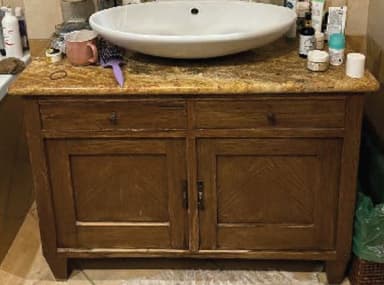 A wooden bathroom vanity featuring a rich brown finish, a speckled granite countertop with an integrated backsplash, and a white ceramic vessel sink. The cabinet has two functional drawers at the top and two cabinet doors below, each adorned with a distinct chevron-like wood grain pattern. Dark metal knobs serve as hardware for both the drawers and doors, complementing the vanity's traditional yet transitional aesthetic. — 3D model