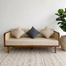 A modern daybed featuring a natural wood frame with cane webbing panels, a thick upholstered seat cushion, and loose throw pillows, designed for both seating and reclining. — 3D model