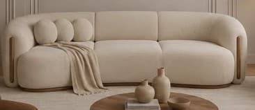 A long, contemporary curved sofa upholstered in a light, textured fabric, featuring a sleek, low-profile design with rounded edges and subtle wooden accents integrated into the base and armrests. Three matching round accent pillows are visible at one end. — 3D model