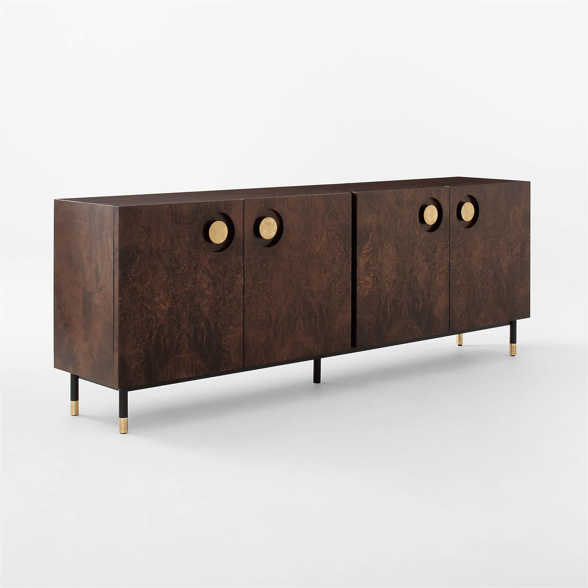 A long, rectangular sideboard with a dark, burl wood veneer finish. It features four doors, each with a circular, brass-toned handle inset into the surface. The unit is supported by four tapered legs, which are black with brass accents at the feet. — 3D model