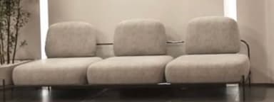 A modern three-seater sofa featuring a minimalist black metal frame that forms the base and supports the backrests. It comprises three individual, light-colored fabric upholstered seat cushions and three matching back cushions, designed without armrests for a streamlined aesthetic. — 3D model