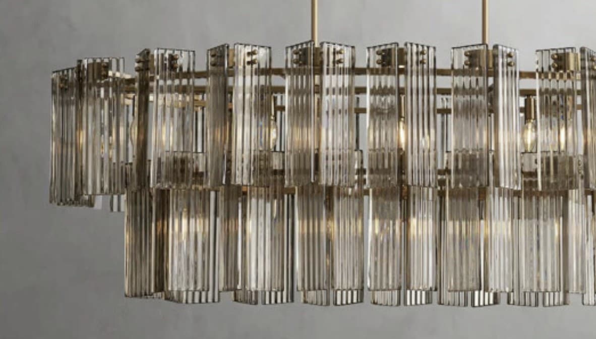 A multi-tiered chandelier featuring numerous vertical, fluted glass rods arranged in concentric circles. The glass elements are suspended from a metallic frame, creating a layered effect. The metallic components appear to be aged brass or a similar warm-toned metal. Several bare incandescent bulbs are visible within the structure, providing illumination. — 3D model
