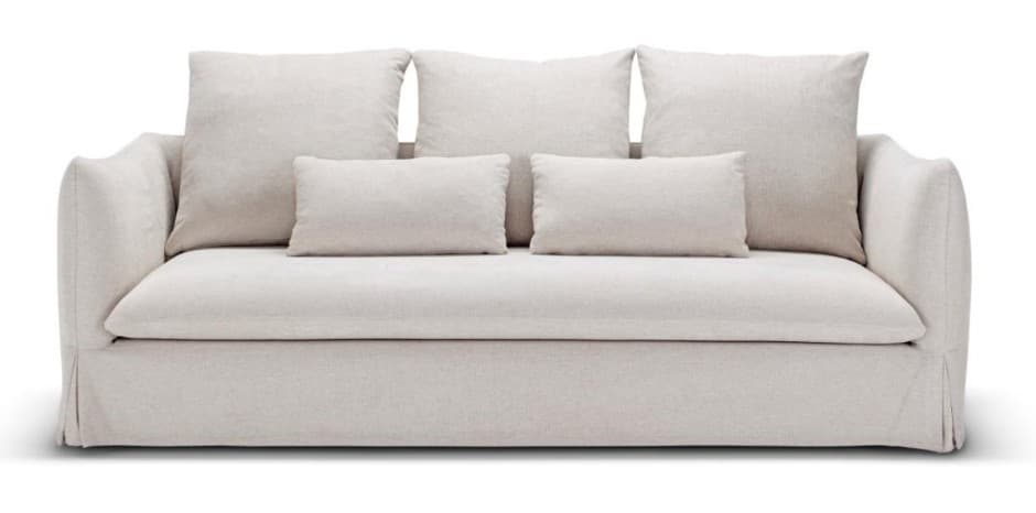 A contemporary sofa featuring a full slipcover in a light, neutral fabric. It has three large square back cushions and three smaller rectangular accent pillows, all loose. The arms are gently rolled or sloped, and the base features a skirted slipcover design. — 3D model