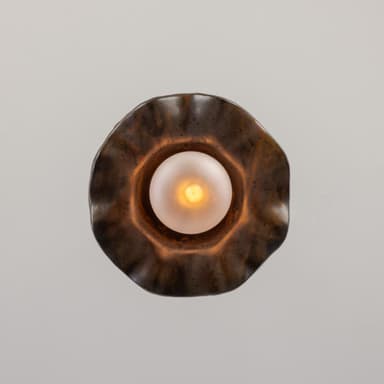 A pendant light featuring a distinctive wavy, shell-like metal shade with a mottled, patinated bronze finish. Suspended beneath the shade is a spherical frosted glass diffuser, emitting a soft, warm light. The fixture hangs from a braided textile cord, connecting to the shade via a small brass fitting. — 3D model