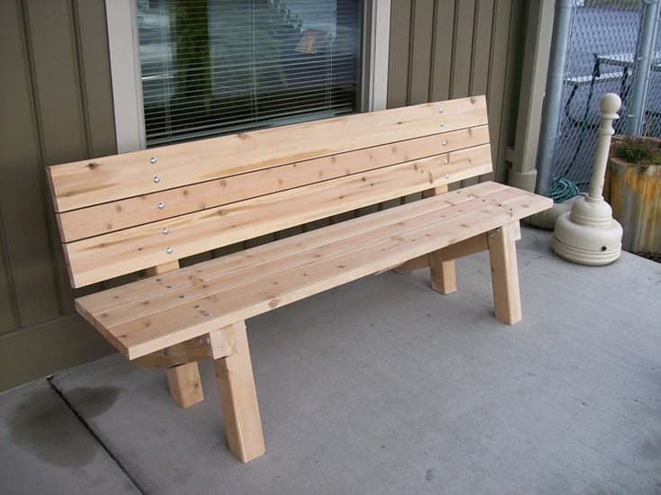 This is a simple, contemporary outdoor bench constructed from light-colored wooden slats and robust rectangular wooden posts, fastened with visible metal hardware. The design features a slatted seat and a slightly angled slatted backrest, supported by two sets of post legs. The natural wood grain is prominent, suggesting a natural finish that highlights the material's inherent beauty. — 3D model