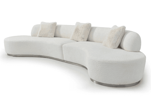 A modern, modular, curved sofa with a textured white upholstery and integrated bolsters. The sofa features a smooth, rounded silhouette with a low-profile metallic base. It is accompanied by three decorative throw pillows with a fluffy, fur-like texture. — 3D model