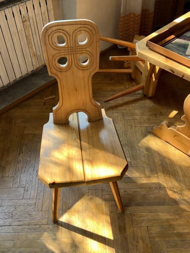 A light-toned solid wood chair featuring a distinctive high backrest with carved geometric patterns and a flat, two-plank seat supported by four splayed, tapered legs. The design has a clear rustic or folk art aesthetic. — 3D model