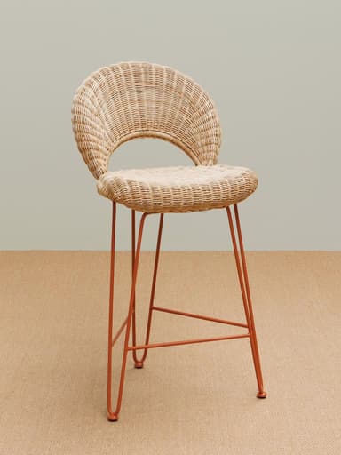 A contemporary bar stool featuring a woven rattan seat and a distinctive curved, open-back rattan backrest, supported by slender, rust-colored metal hairpin legs with an integrated footrest. — 3D model
