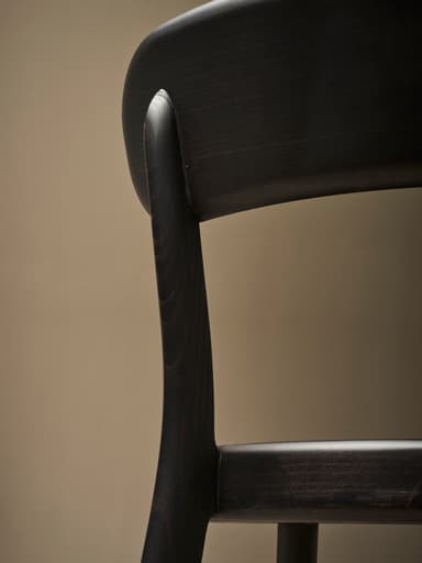 A dark-colored wooden dining chair viewed from the back. The chair features a gently curved backrest supported by two upright posts that extend from the seat. The seat itself is also curved and appears to be solid. The legs are slightly tapered and angled outwards. The overall construction suggests a modern or contemporary design with clean lines and a minimalist aesthetic. — 3D model