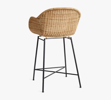 A bar stool featuring a natural woven rattan seat and backrest with integrated armrests, supported by a minimalist black metal frame with an X-shaped footrest. — 3D model