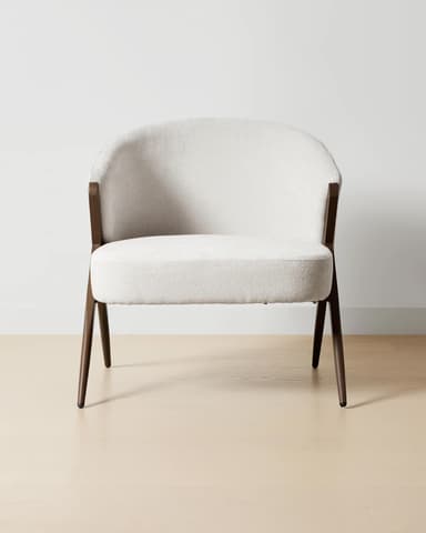 A modern armchair with a rounded back and seat, upholstered in a textured off-white fabric. The frame and legs are made of dark wood, featuring an angular, open design that supports the upholstered shell. — 3D model