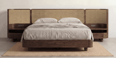 A modern platform bed featuring a dark wood frame with rounded edges and a prominent headboard constructed from multiple cane panels. The headboard design includes integrated floating nightstands on either side, which also have rounded forms and a single drawer. The bed is depicted with light-colored bedding, complementing the natural cane and dark wood. — 3D model