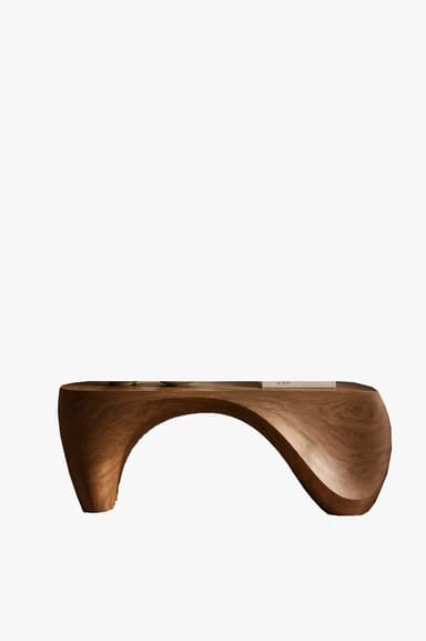 A long, low, sculptural coffee table crafted from what appears to be solid walnut wood. It features a continuous, curved form that acts as both top surface and support, creating a bridge-like structure. The top surface includes two distinct, circular recessed areas, likely intended for holding drinks or small objects. The wood exhibits a rich, dark brown tone with visible grain, and the design is characterized by smooth, organic lines. — 3D model
