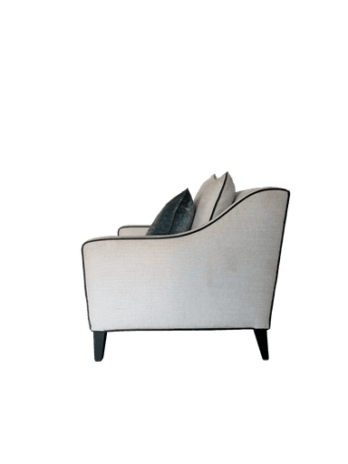 A contemporary upholstered armchair featuring a light, textured fabric and dark contrasting piping. It has a deep seat, padded armrests, and comes with a matching back pillow and a dark green velvet throw pillow. The chair is supported by dark, low-profile tapered legs. — 3D model