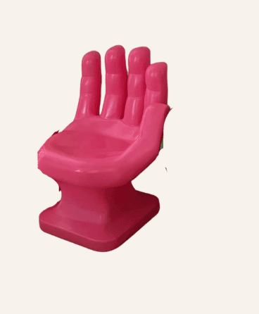 A vibrant pink novelty chair designed in the shape of an upright human hand. The fingers form the backrest, curving slightly to provide support, while the palm serves as the seat. The chair is crafted from a smooth, molded material, likely plastic, with a solid, sculptural base for stability. — 3D model