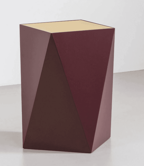 A geometric side table with a faceted, angular design. The main body is a deep plum or burgundy color, featuring sharp planes that create a multifaceted appearance. The top surface is a flat, hexagonal shape with a lighter, possibly brass or gold-toned finish, contrasting with the darker body. The table stands on a flat base. — 3D model