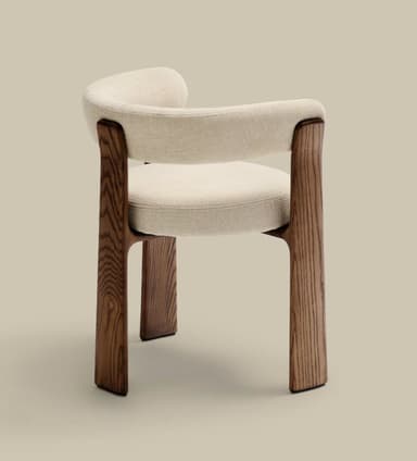 A modern armchair featuring a sculpted dark wood frame and cream-colored textile upholstery. The chair has a rounded, continuous backrest and armrests, and a circular seat cushion. The robust, splayed wooden legs provide a stable and aesthetically integrated base. — 3D model