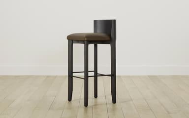 A modern bar stool featuring a dark stained wooden frame and a padded, upholstered seat with a low backrest. The stool has four sturdy, slightly tapered legs and an integrated metal footrest. — 3D model