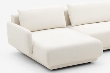 A modular sectional sofa with a chaise lounge extension. The sofa features a low-profile design with thick, upholstered cushions and rounded armrests. The frame appears to be upholstered in a textured fabric. — 3D model