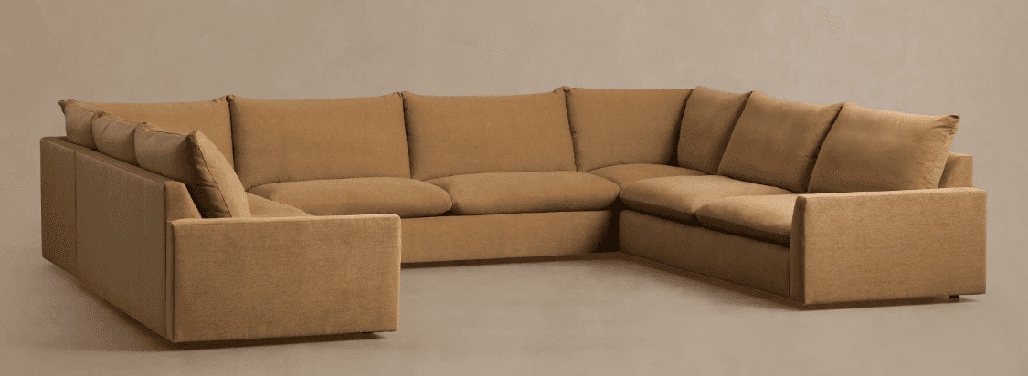 A large, U-shaped sectional sofa upholstered in a neutral brown/tan fabric. The sofa features a low-profile design with thick, plush seat cushions and supportive back cushions. Its arms are wide and flat, maintaining a clean, contemporary aesthetic. The modular construction allows for a sprawling seating arrangement suitable for multiple occupants. — 3D model