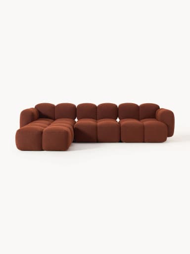 An L-shaped modular sectional sofa composed of individual square and rectangular blocks, upholstered in a rust-colored textured fabric. The design features a low profile and rounded edges on each block, creating a plush, inviting appearance. The sofa is configured with a chaise extension on the left side when viewed from the front. — 3D model