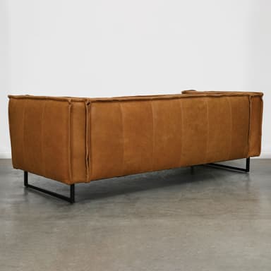 A contemporary three-seater sofa featuring tan-colored, possibly distressed leather upholstery and a minimalist black metal sled base. The sofa has wide, squared-off armrests and back, with visible piping and stitching details defining the cushions and edges. The overall aesthetic is modern and streamlined. — 3D model