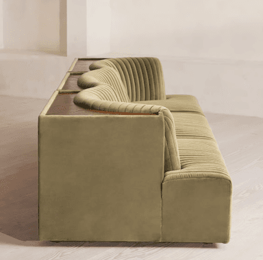 A long, contemporary sofa with a channeled upholstery design. The sofa features a modular appearance with distinct sections, creating a sense of depth and texture. It has a low profile and a deep seat, with curved armrests or side panels. A small, dark wood-toned surface is visible on the far left side, integrated into the structure. — 3D model