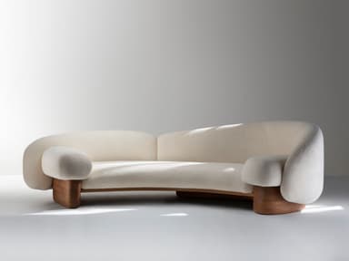 A modern, curved sofa featuring cream-colored bouclé upholstery and a distinctive, sculptural dark wood base. The design emphasizes organic forms with rounded edges and integrated arms. — 3D model