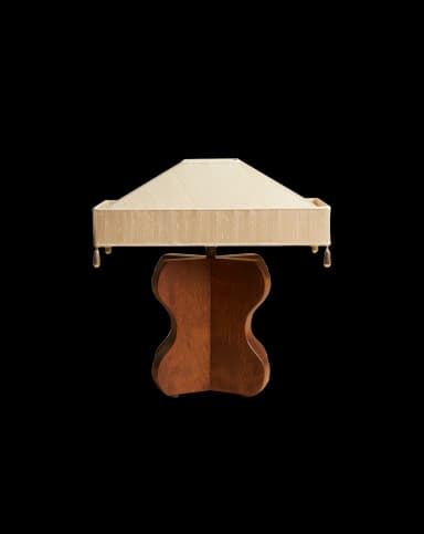 A table lamp featuring a distinctive sculpted wooden base in a dark finish and a rectangular, tapered fabric shade with pleated details and decorative tassels at the corners. The base exhibits an organic, hourglass-like form. — 3D model