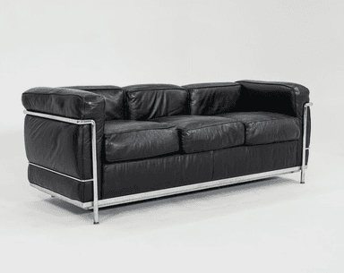 A three-seater sofa characterized by its boxy, geometric silhouette and exposed tubular chrome-plated steel frame. It features black leather upholstery on separate, plump cushions for the seat, back, and arms. The cushions appear to be removable and are designed to sit within the sturdy metal structure. The leather shows signs of use, such as creasing, indicating a well-loved piece. — 3D model