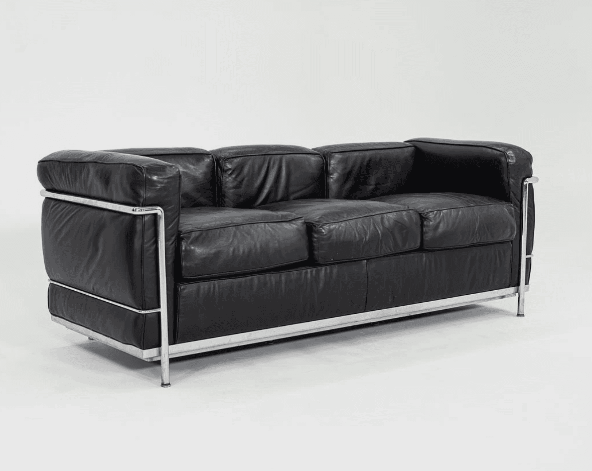 A three-seater sofa characterized by its boxy, geometric silhouette and exposed tubular chrome-plated steel frame. It features black leather upholstery on separate, plump cushions for the seat, back, and arms. The cushions appear to be removable and are designed to sit within the sturdy metal structure. The leather shows signs of use, such as creasing, indicating a well-loved piece. — 3D model