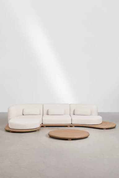 A modular sectional sofa with a curved chaise lounge on one end. The sofa features a light-colored upholstered body and loose back cushions. The base and accents are made of light-colored wood, with a slatted design on the extended side panel. A circular, low-profile coffee table with a slatted wooden top is positioned in front of the sofa. — 3D model