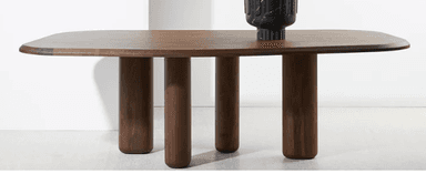 A contemporary dining table with a distinctive design featuring a smooth, dark wood tabletop and four cylindrical legs. The tabletop has rounded corners and a subtle curvature. The legs are thick and have a rounded profile, providing a sturdy base. A decorative black vase is placed on the table. — 3D model