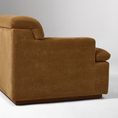A close-up view of the armrest and side of a sofa. The sofa is upholstered in a textured, woven fabric with a brown hue. It features a rounded armrest that extends upwards and a rectangular base constructed from wood. — 3D model