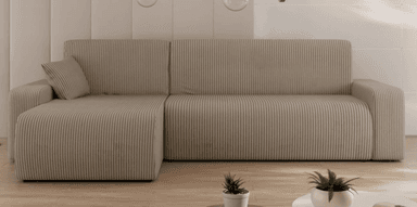A modular sectional sofa with a chaise lounge extension. The sofa features a ribbed upholstery texture and rounded edges on its frame and armrests. A single matching throw pillow is visible on the chaise section. The sofa is upholstered in a light brown or beige fabric. — 3D model