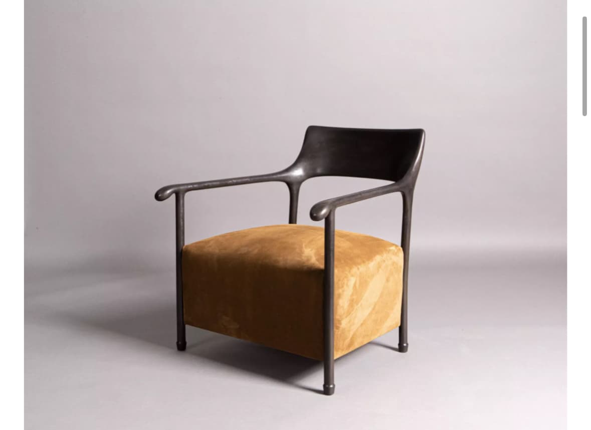 A modern armchair with a dark, possibly metal, frame and a plush, textured seat cushion. The frame has a minimalist design with smooth, curved armrests that flow into the backrest. The seat is upholstered in a mustard-yellow fabric with a distinct wavy pattern. — 3D model