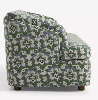 A three-seater sofa with a rounded armrest on the left side. The sofa is upholstered in a fabric with a repeating floral pattern in green, blue, and white. It has a solid base and short, wooden legs. — 3D model