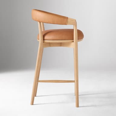 A bar stool with a curved backrest and armrests, featuring a wooden frame and leather upholstery for the seat and back. The frame consists of four cylindrical legs connected by stretchers for stability. The seat is flat and padded, while the backrest is also upholstered and curves to provide lumbar support. The armrests are integrated into the frame structure. — 3D model