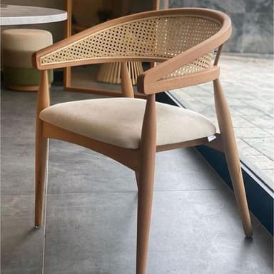 A modern dining armchair constructed from light-toned wood with a curved, open backrest featuring cane webbing. The seat is upholstered in a light, neutral fabric, and it stands on four subtly tapered wooden legs. — 3D model