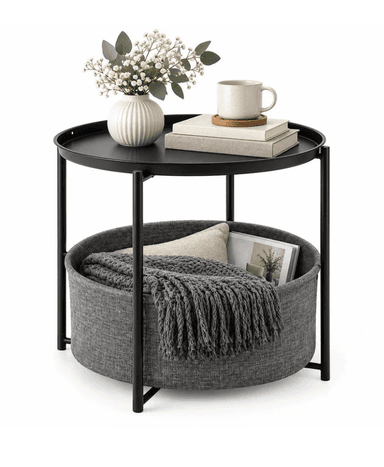 A modern round side table featuring a black metal frame and a black tray-style tabletop. Below the tabletop, a large, round, gray fabric basket is integrated into the frame, designed for storage. The table sits on four slender black metal legs. — 3D model