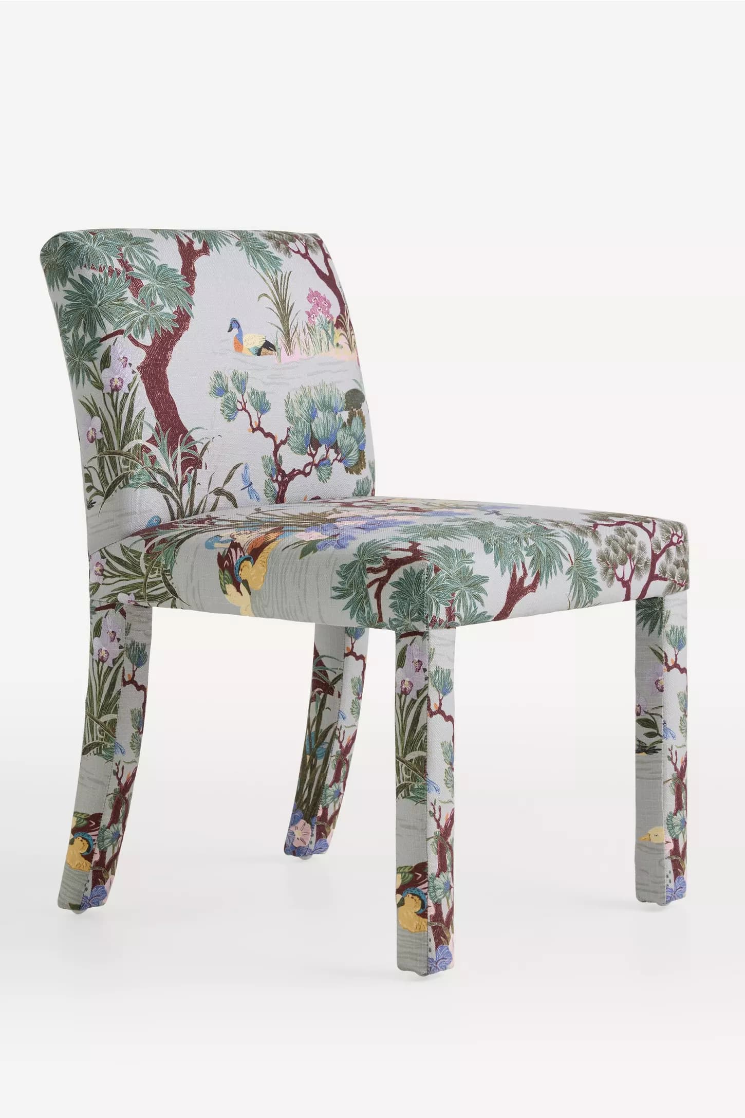 The image displays a fully upholstered armless side chair, presented against a plain white background. The chair features a gently curved backrest and a flat seat, with all visible surfaces, including the four legs, covered in a light blue-green fabric. This fabric is adorned with a detailed, multi-colored scenic botanical and wildlife pattern, depicting trees, lush foliage, various flowers, and diverse birds and insects. The front legs are straight, while the rear legs exhibit a slight taper, contributing to the chair's stable and elegant profile. The upholstery is meticulously applied, creating a smooth and continuous surface that emphasizes the intricate pattern as the primary design element. — 3D model