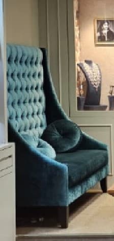 A high-back armchair upholstered in a teal or turquoise velvet-like fabric, featuring deep button tufting on the backrest and two matching spherical accent pillows. The chair has a sleek, contemporary wingback profile and is supported by dark wooden legs. — 3D model