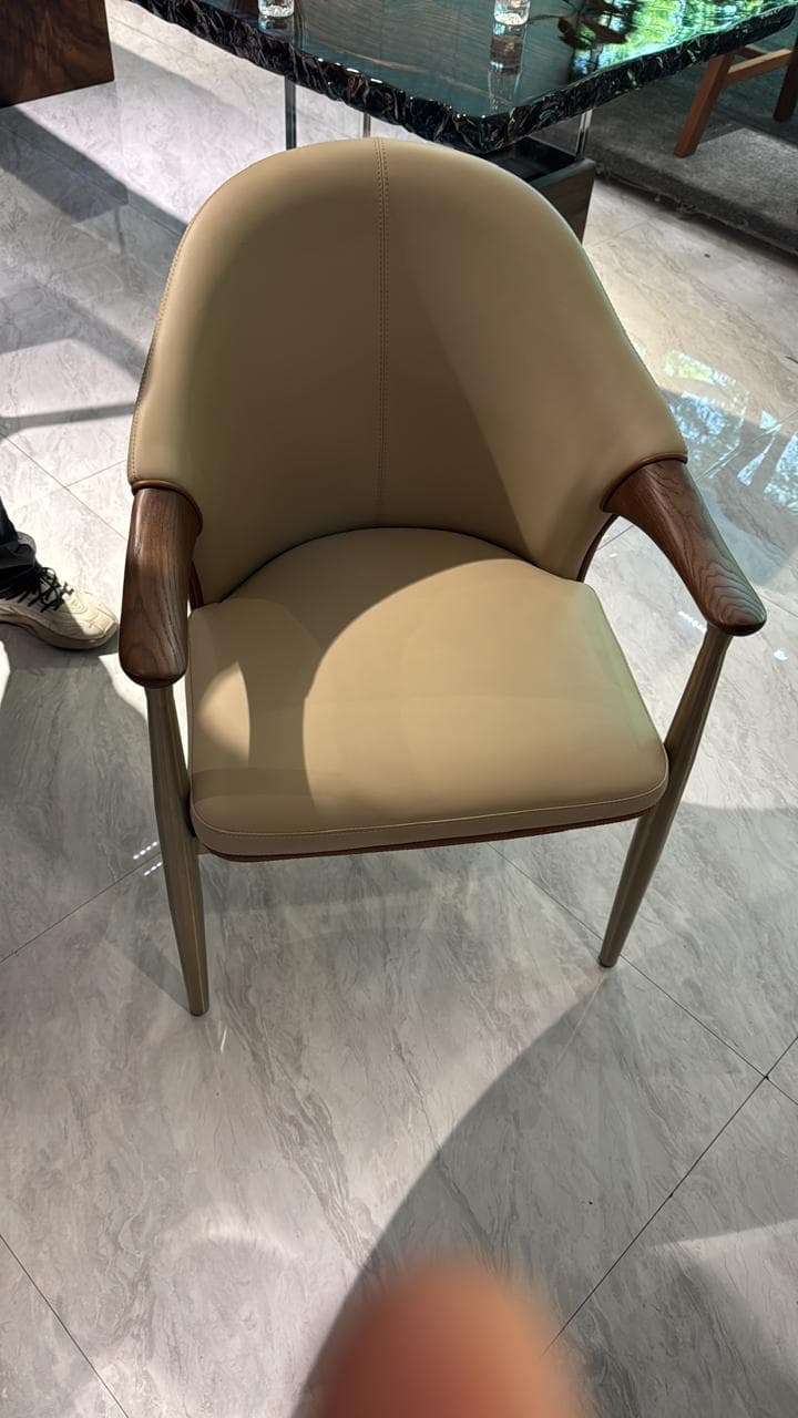 A modern armchair featuring a curved, upholstered backrest and seat in a neutral-toned leather. The frame and armrests are constructed from wood, exhibiting a smooth finish and natural grain. The design incorporates clean lines and a minimalist aesthetic. — 3D model