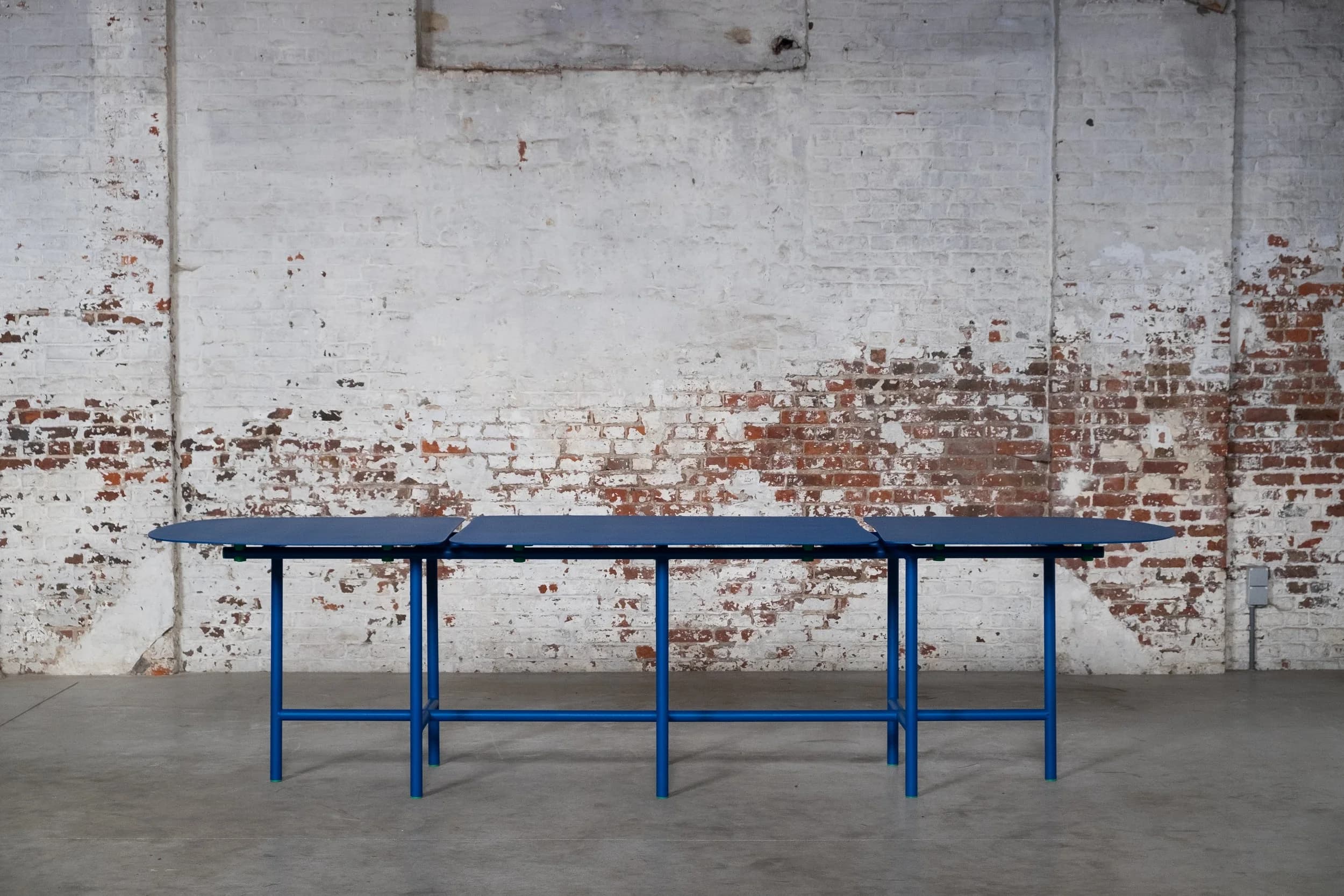 A long, modular dining table featuring three distinct segments with rounded ends, supported by a vibrant blue tubular metal frame. Each segment's top is dark blue, complementing the bright blue base, with small green connectors and feet accents. — 3D model