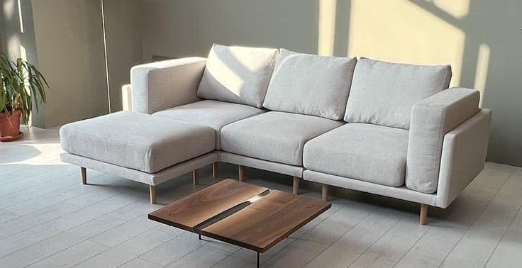A modern L-shaped sectional sofa with a left-hand facing chaise, upholstered in light beige fabric, featuring clean lines, block arms, and subtle tapered wooden legs. — 3D model