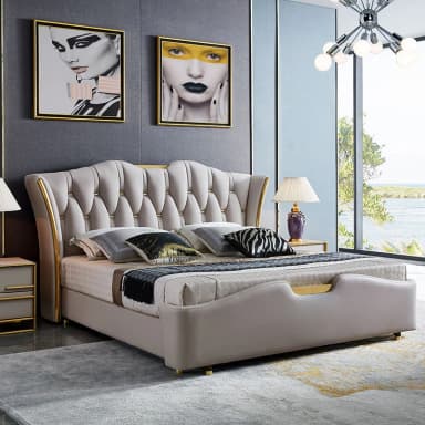 A luxurious contemporary upholstered bed frame with a distinctive wingback headboard. The headboard features deep button tufting in a beige, soft-pile fabric, accented with elegant gold-finished metal trim. The entire bed frame, including the low-profile, subtly curved footboard and side rails, is upholstered in the same beige fabric. It stands on small, gold-finished cylindrical feet. — 3D model