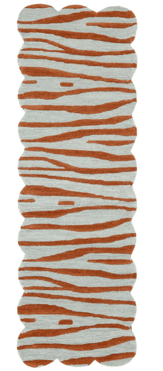 An elongated runner rug with a distinctive scalloped edge, featuring an abstract animal print pattern. The primary colors are a muted light blue and a vibrant terracotta orange, resembling a stylized tiger or zebra stripe. The rug appears to have a soft, cut pile texture. — 3D model